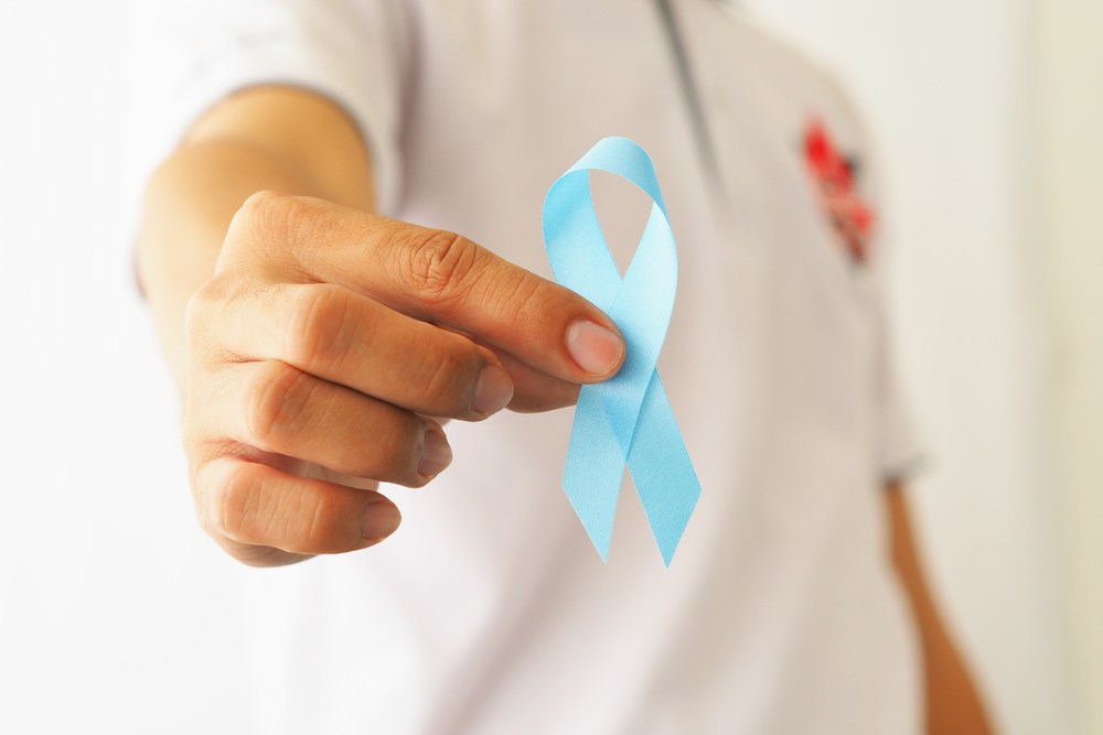 male hand holding blue prostate cancer awareness ribbon.