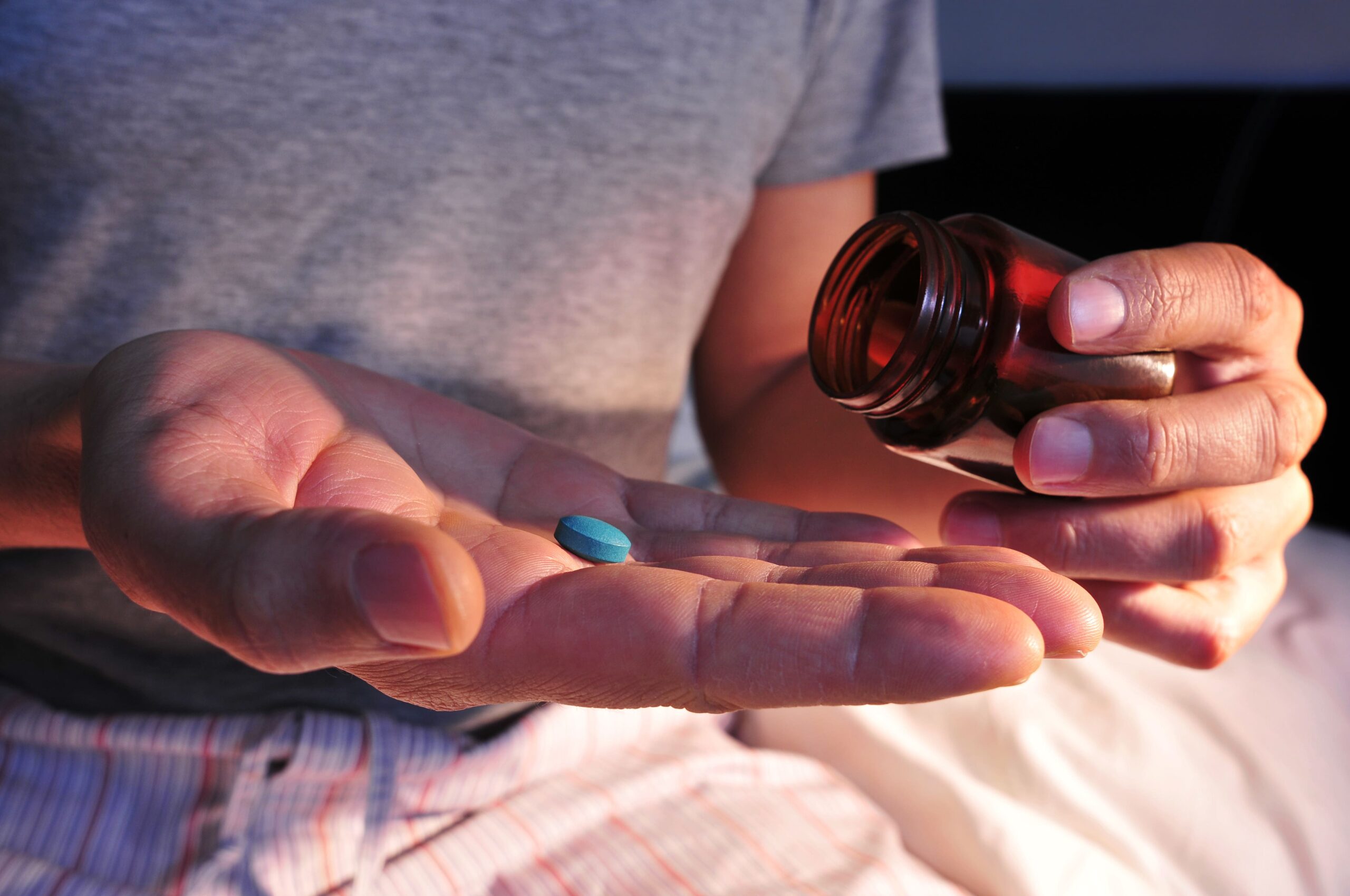 man taking a blue pill out of a container.